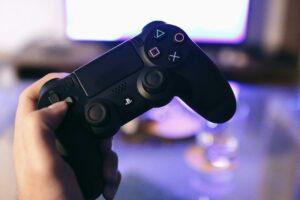 Person holding a gaming controller, blurred screen in background.