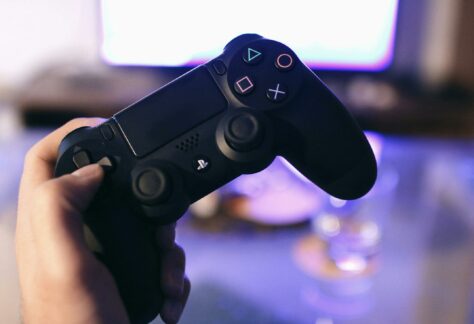 Person holding a gaming controller, blurred screen in background.