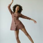 Elegant young woman with curly hair dancing gracefully in a brown dress, embodying beauty and empowerment.